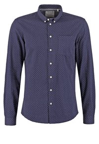 Chemise bleu marine à manches longues avec des boutons, à pois blancs, col boutonné, poche poitrine et boutons blancs sur le devant.