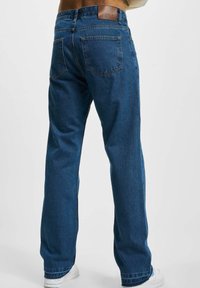 Jeans de mezclilla azul con corte recto, parche de cuero en la cinturilla y dos bolsillos traseros. La tela tiene una textura suave y un lavado medio.