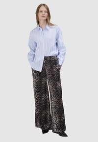 Lichtblauwe gestreepte button-up shirt gecombineerd met wijde leopardprint broek; heeft een zachte stof en een ontspannen pasvorm. Zwarte puntige schoenen.