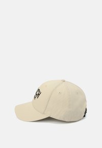 Beige baseballkeps tillverkad av textil med struktur, med svarta bokstäver, en böjd skärm och ett justerbart band bak.