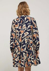 Robe à motifs floraux avec manches longues, base bleu marine et designs contrastants en pêche et crème. Ourlet évasé avec des couches superposées ; tissu léger.