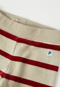 Beige-housut, joissa on punaisia vaakaraitoja, joissa on teksturoitu kangas, ribbikuitu vyötärö ja pieni ommeltu etiketti, jossa on "P."