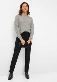 Maglione grigio a maglia con finitura testurizzata, pantaloni neri su misura e una pochette plissettata nera. Stivaletti a lunghezza caviglia dal taglio slim completano l'outfit.