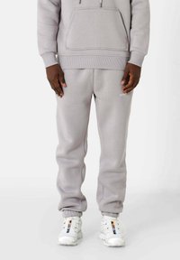 Sweat-shirt gris clair avec poche avant et joggeurs assortis, présentant une coupe décontractée et des chevilles resserrées, associés à des baskets blanches.