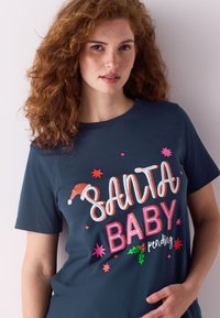 Temno modra bombažna majica s pisanim vezenim napisom "SANTA BABY pending" ter motivom božičkove kape in zvezdnih vzorcev. Kratki rokavi in okrogel izrez.