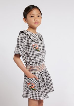 Robe vichy en gris et blanc, dotée d'un col froncé, d'une taille smockée et de patches de fleurs brodées sur la poitrine et la poche.