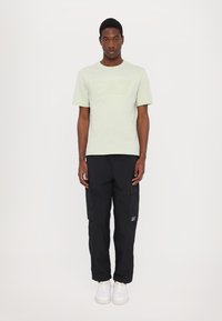 T-shirt vert clair à manches courtes avec logo EA7 en relief, associé à un pantalon cargo noir avec poches latérales et des baskets blanches.