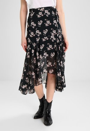 Jupe portefeuille noire à motifs floraux avec des fleurs roses, fabriquée en tissu léger. Elle présente un ourlet asymétrique et un design superposé, associée à des bottes noires.