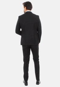 Giacca e pantaloni neri con un design aderente, texture liscia e cuciture dettagliate. Presenta un colletto bianco e scarpe nere lucide.