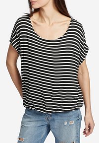 Camiseta de rayas blancas y negras con escote redondeado y mangas cortas, hecha de una tela suave. Usada sobre unos vaqueros de mezclilla desgastados.