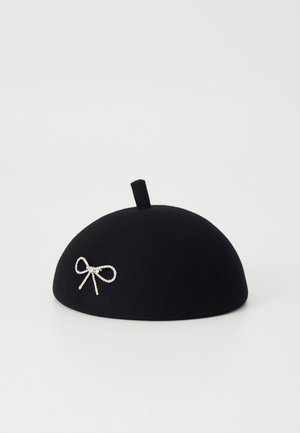 Béret de lã preto com uma forma achatada e arredondada, apresentando um pequeno botão superior e um laço decorativo de strass na frente.