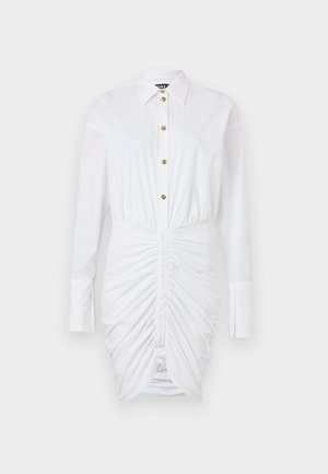 Balta kleita ar garām piedurknēm, pogām priekšpusē, ar zeltītām pogām un savelkošu tekstūru gar malām, veidojot pieguļošu siluetu.