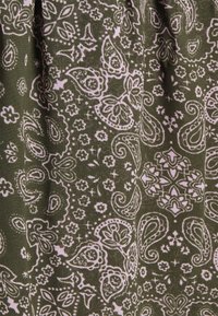 Tecido verde com um padrão paisley em branco, apresentando acentos florais e um detalhamento intrincado por todo o tecido. A textura parece suave.