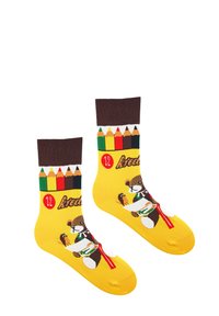 Żółte skarpetki z wzorem brązowego niedźwiedzia trzymającego kanapkę, z brązowym prążkowanym mankietem i kolorowym wzorem ołówków u góry.