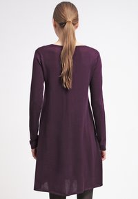 Robe à manches longues en tissu tricoté violet profond, présentant une coupe décontractée et un léger effet scintillant. Le dos possède un col arrondi et une texture lisse.