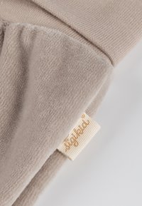 Beige Fleece-Decke mit strukturierter Oberfläche, mit umgeschlagenem Rand und einem kleinen beigen Etikett mit goldener Schrift, das in den Stoff eingenäht ist.