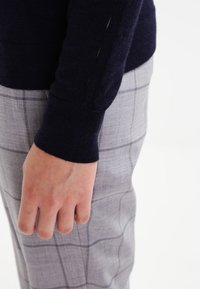 Marinblått stickat tröja med ribbade muddar och sidofickor, ihop med ljusgrå rutiga byxor med en texturerad yta och slät tyger.