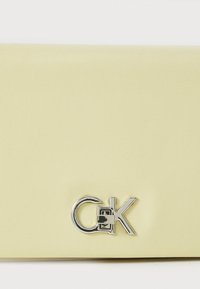 Yellow textured leather wallet with a metal logo accent. Smooth finish, rectangular shape, featuring a clasp detail. Compact design.