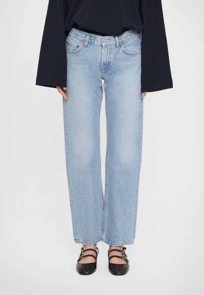 Hellblaue Denim-Hose mit weitem Bein und hoher Taille, ausgestattet mit fünf Taschen und dezenten Auswaschungen. Kombiniert mit schwarzen, trageflächigen Sandalen.