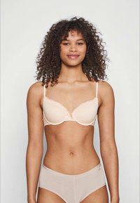 Beige polstret bh med bølget blondekant og justerbare stropper, kombinert med gjennomsiktige beige truse. Glatt tekstur og enkelt design.