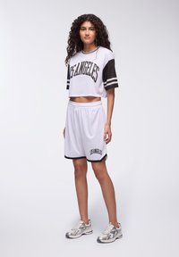 Top corto in rete bianca con maniche nere e scritta "LOS ANGELES", abbinato a pantaloni corti bianchi con dettagli neri e vita nera.