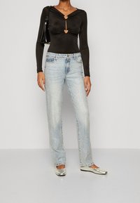 Body a maniche lunghe nero con ritagli a forma di cuore, abbinato a jeans chiari decorati con strass argentati. Il modello indossa ballerine argentate.