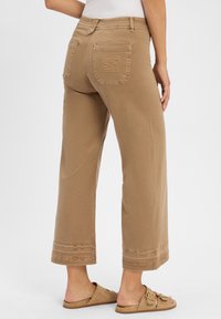 Pantaloni larghi color khaki realizzati in un tessuto morbido, dotati di tasche anteriori e posteriori, con cuciture decorative all'orlo.
