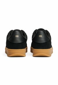 Zapatillas negras de cuero y ante, con un upper texturizado negro, logo con acento dorado y una suela de goma marrón claro.