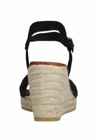 Black wedge sandal with a textured jute heel, adjustable ankle strap, and brown inner lining. Features a layered, woven design.