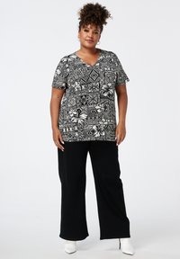 Kort-vingerige zwart-wit patroon top met bloem- en geometrische ontwerpen, gecombineerd met losse zwarte broek en witte enkellaarzen.