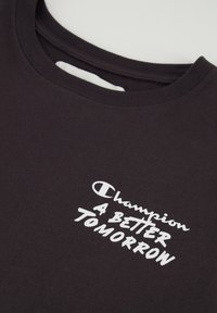 Camiseta de algodón negra con cuello redondo, con texto blanco que dice "Champion A BETTER TOMORROW" y textura de tela suave.