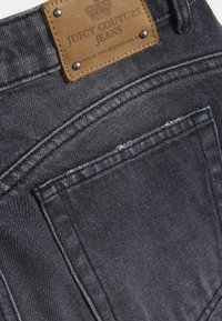 Σκούρο τζιν με υφή, με καφέ δερμάτινο σημείο που φέρει την ετικέτα "Juicy Couture Jeans" και δύο πίσω τσέπες.