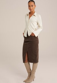 Cămașă crem cu dungi, cu mâneci lungi, asociată cu o fustă din material de catifea închisă, cu o fanta frontală, și cizme bej până la genunchi.