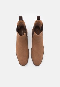 Bottes chelsea en daim marron à la cheville avec des panneaux latéraux élastiques et des languettes de tirage, vues de dessus sur un fond blanc.