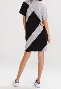 Kvinna som bär en kortärmad klänning ovanför knä med svarta och grå diagonala färgblock, i kombination med vita Adidas-sneakers.