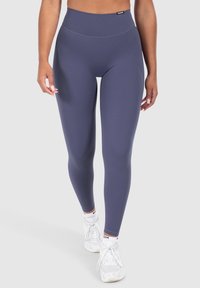 Leggings a vita alta in tessuto blu scuro. Texture liscia con una vestibilità elastica. Abbinati a scarpe da ginnastica bianche. Branding minimale sulla vita.