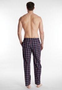 Pantalones de pijama a cuadros en azul marino con rayas rojas y blancas, con una cinturilla elástica y bolsillos laterales. Tela suave con un corte relajado.