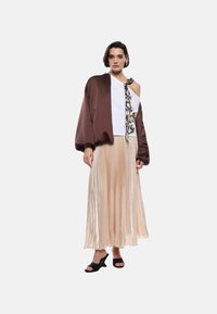 Giacca bomber in satin marrone, top bianco off-shoulder, gonna maxi plissettata beige, sandali neri con tacco, sciarpa con stampa leopardata in accent.