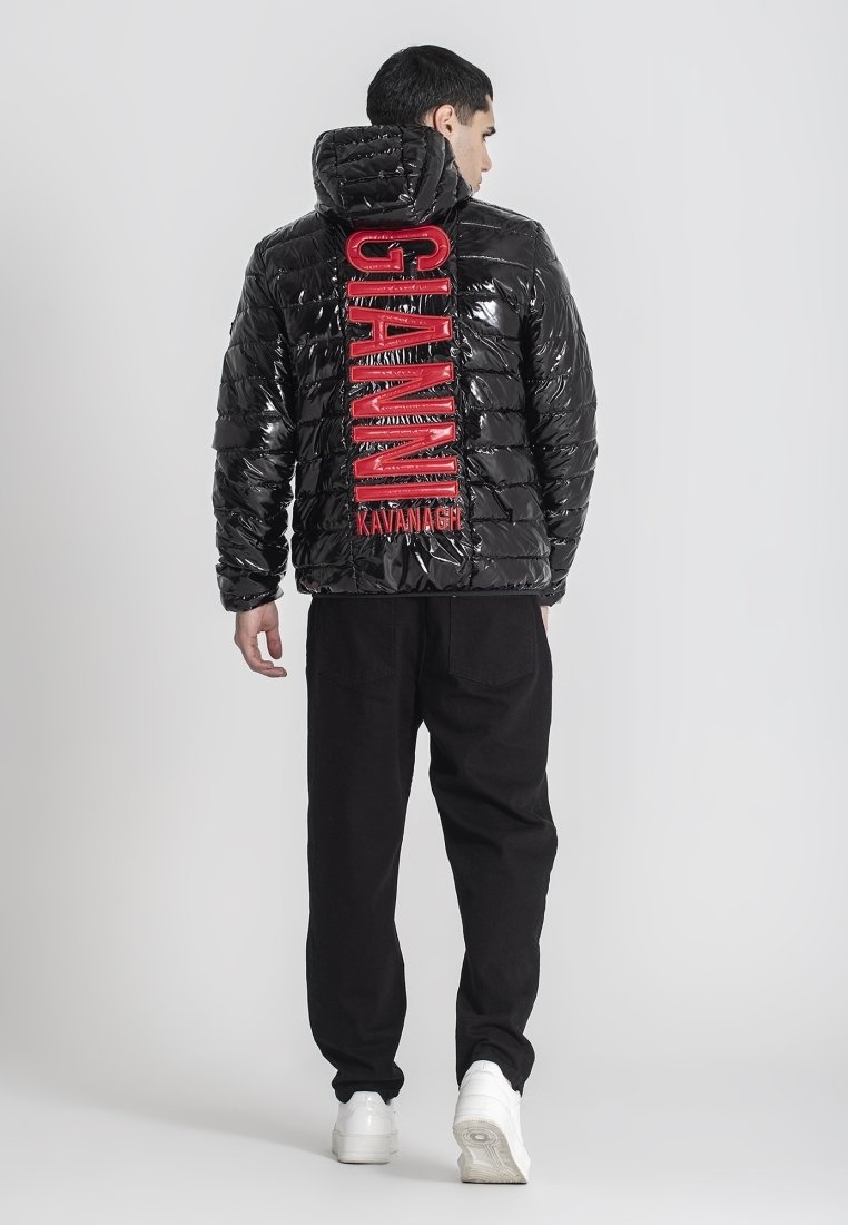 Uomo girato di spalle che indossa un giubbotto a vento nero lucido con testo rosso "GIANNI KAVANAGH" sulla schiena, pantaloni neri e sneakers bianche.