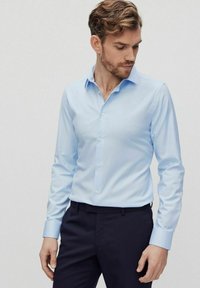 Lichtblauw langemouwen overhemd van gladde katoenen stof, met een puntige kraag, knoopsluiting en manchetten met een slim fit, gecombineerd met donkere broek.