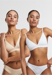 Deux bralettes en beige et blanc, avec un tissu doux, des bonnets triangulaires, des bretelles fines et un design sans couture. La paire blanche présente des accents en dentelle.