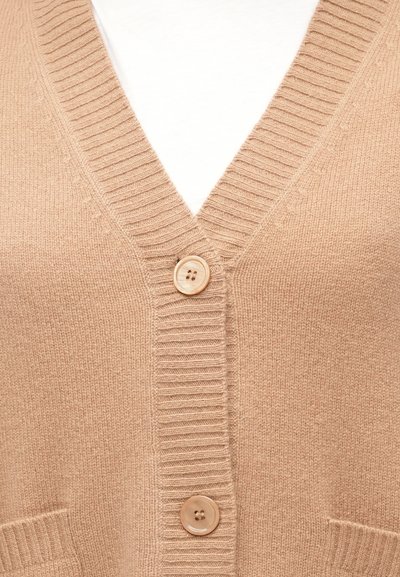Μπεζ πλεκτή ζακέτα με V-λαιμόκοψη, ριμπ τελείωμα, δύο εμπρόσθιες τσέπες και μία μεγάλη κουμπιά για κλείσιμο. Απαλή υφή, casual σχεδιασμός.