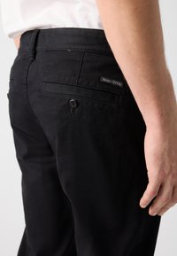 Mustad puuvillased püksid, millel on kitsas lõige, tagakotid, ühe nööbi detail ja väike "Marc O'Polo" silt vööl.