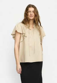 Beige-randig blus med fladdrande ärmar, lättviktsmaterial, knappstängd halsringning och dragsko-detalj. Bärs över en svart outfit.