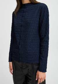 Chemise long à manches longues bleu marine texturée avec un motif tissé, dotée d'un col montant et d'une fermeture à boutons, associée à un pantalon en cuir noir.