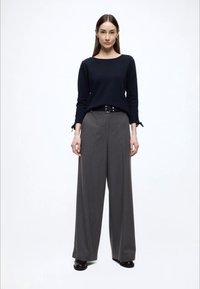 Granatowa długi rękaw bluzka z teksturowaną tkaniną i subtelnymi detalami, zestawiona z szarymi, wysokim stanem i szerokimi nogawkami spodniami oraz czarnymi butami.