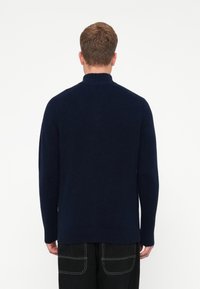 Maglione lavorato a maglia blu navy con colletto alto, polsini e orlo a coste. Presenta un design senza cuciture e una texture morbida. Vista posteriore mostrata.