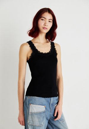 Black tank top featuring a scalloped lace trim around the neckline and arms, made of soft fabric, paired with light blue denim jeans.