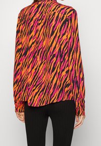 Zwarte langemouwen shirt met gedurfde oranje en roze tijgerstrepen, voorzien van een ronde zoom en met knoopmanchetten, gemaakt van lichtgewicht stof.