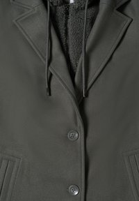 Giacca verde con cappuccio, interna in peluche, tessuto esterno testurizzato, due bottoni e cappuccio regolabile. Presenta rever sagomati e dettagli laterali.